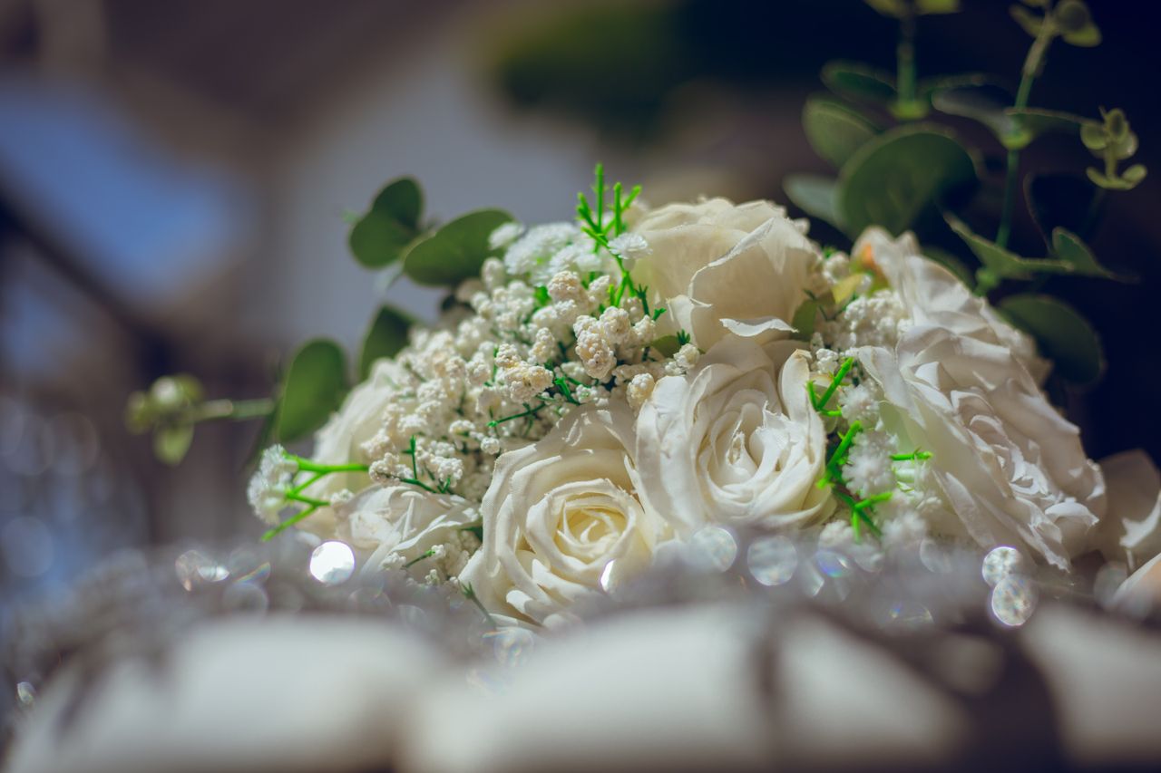 Close-up of a delicate white rose bridal bouquet with greenery, captured in a soft focus.