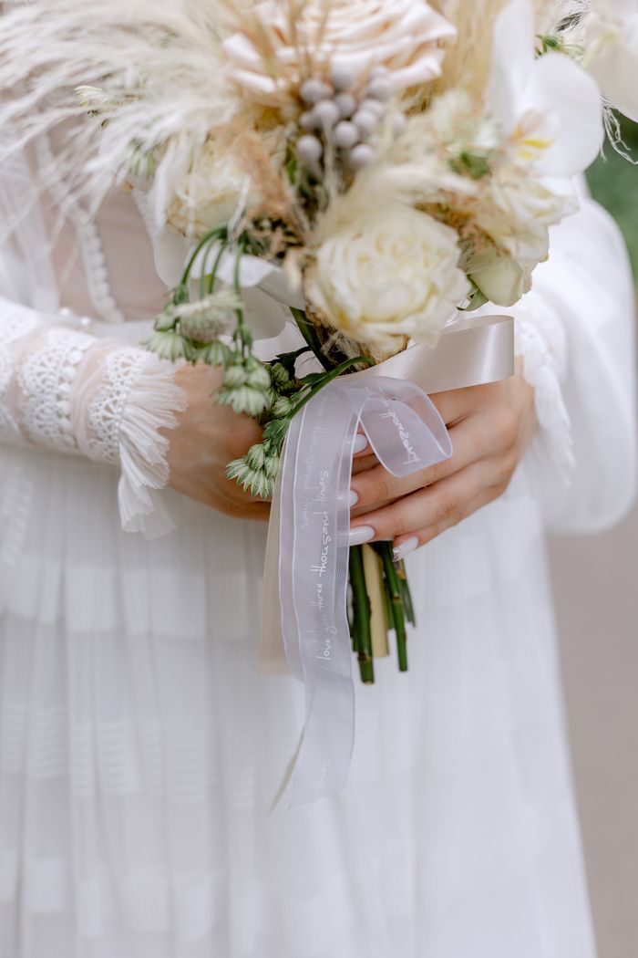 Close-up of a bride holding an elegant white rose bouquet with delicate ribbon.